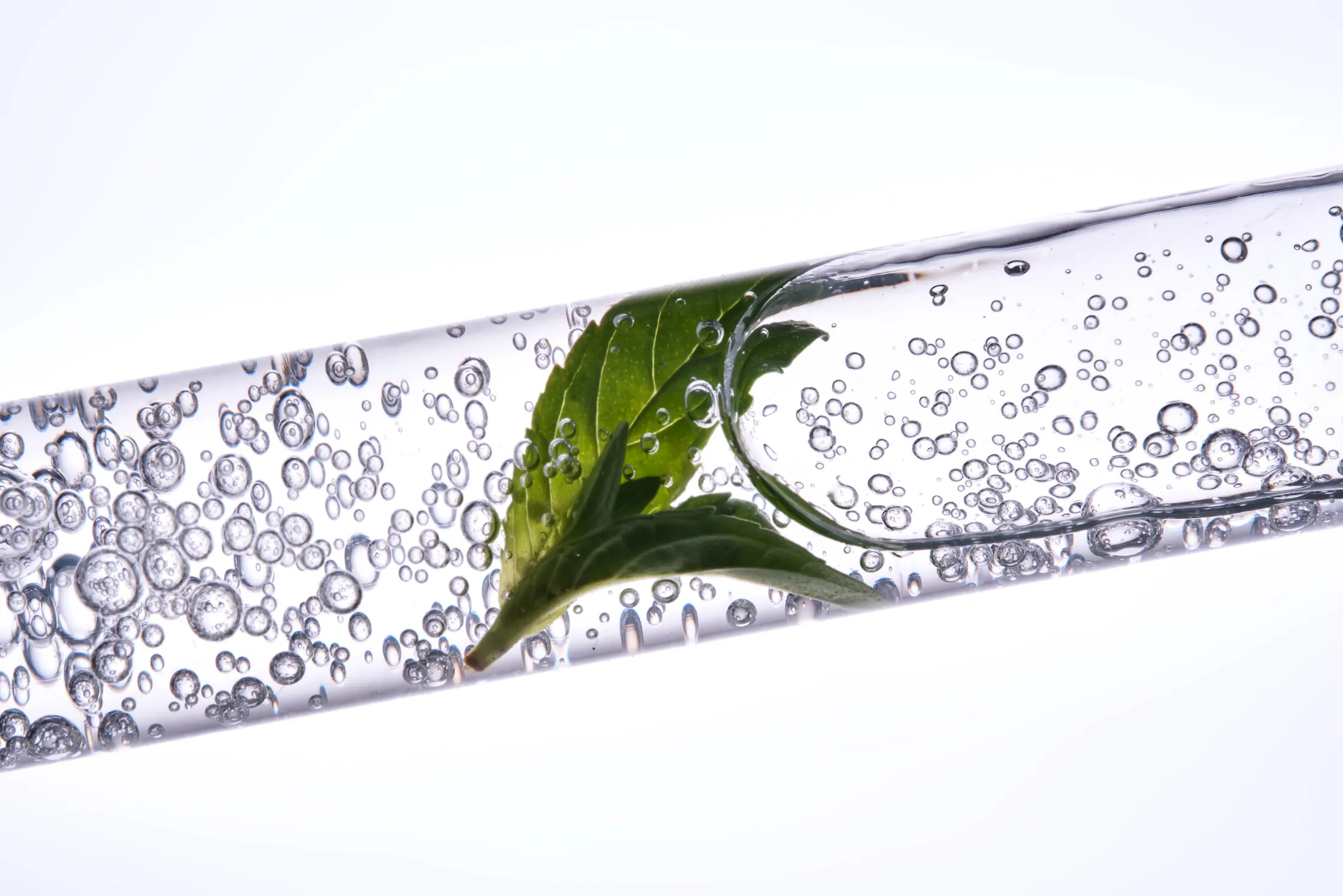 A fresh green botanical leaf suspended in a clear, bubbling serum